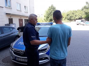 37- letni mężczyzna podejrzewany o stosowanie przemocy wobec żony. Policjant z komisariatu w Konstancinie - Jeziornie doprowadza go do policyjnego radiowozu.