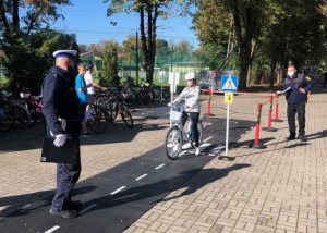 Policjant i strażnik znajdują się na placu, gdzie uczniowie odbywają egzamin na kartę rowerową