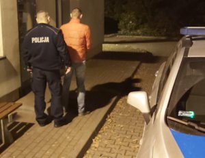 Policjant wraz z zatrzymanym mężczyzną w pomarańczowej kurtce