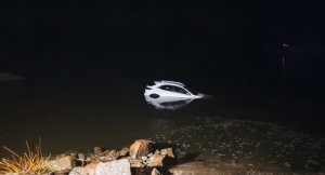Biały samochód częściowo zanurzony w wodach Wisły. Zdjęcie ciemne.