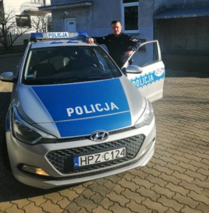 Umundurowany policjant przed oznakowanym radiowozem