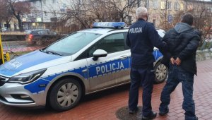 Umundurowany policjant stoi przy oznakowanym radiowozie wraz z zatrzymanym mężczyzną