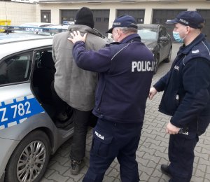 Umundurowani policjanci wprowadzają do oznakowanego radiowozu mężczyznę