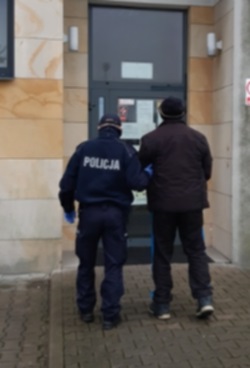 Umundurowany policjant wprowadza zatrzymanego do budynku sądu