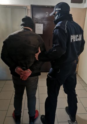 Umundurowany policjant prowadzi zatrzymanego mężczyznę przez pomieszczenia komisariatu