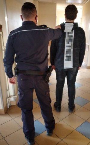 Umundurowany policjant przeprowadza zatrzymanego mężczyznę przez korytarz komisariatu