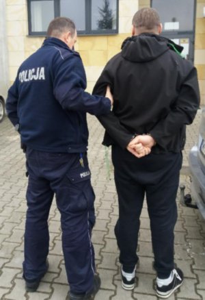 Umundurowany policjant z zatrzymanym mężczyzną przed budynkiem sądu