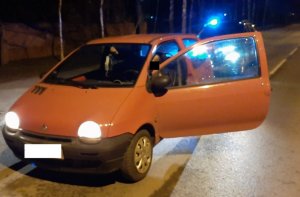 Samochód koloru pomarańczowego zatrzymany do kontroli, za nim źle widoczny policyjny radiowóz