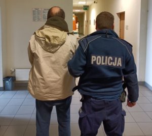 Umundurowany policjant prowadzi korytarzem zatrzymanego mężczyznę w jasnej kurtce