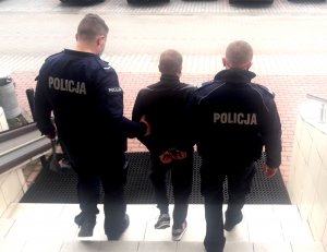 Policjanci wyprowadzają z budynku komendy mężczyznę podejrzewanego o stosowanie przemocy