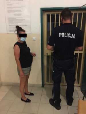 Umundurowany policjant stoi wraz zatrzymaną kobieta przed wejściem do policyjnego aresztu