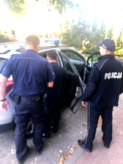 Policjanci umundurowani wraz z zatrzymanym przed policyjnym radiowozem