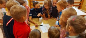 Policjantka w sali przedszkolnej prezentuje zabezpieczanie śladów po przestępstwie