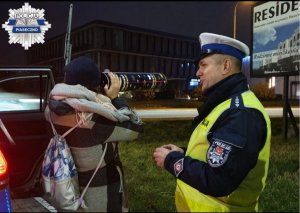 Policjant wydziału ruchu drogowego podczas rozmowy z mieszkanką Piaseczna, prezentuje jak widoczny jest pieszy z odblaskami i bez