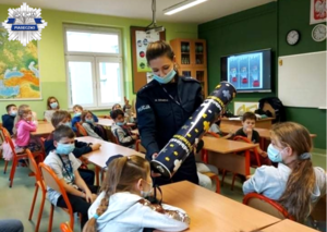 Policjantka przy pomocy "magicznej tuby" pokazuje różnicę w widoczności pieszego posiadającego elementy odblaskowe oraz tego, który ich nie posiada