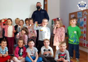 Pamiątkowe zdjęcie po spotkaniu z przedszkolakami na którym są dzieci z odblaskami oraz policjant