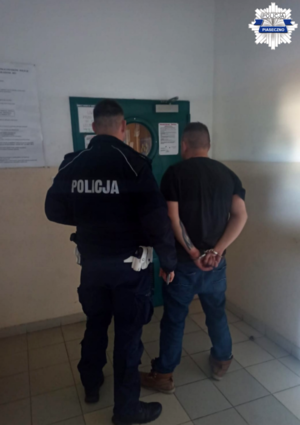 policjant wraz z zatrzymanym mężczyzną przed wejściem do pomieszczenia dla osób zatrzymanych