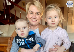 Pani Ewa trzyma na kolanach dwójkę dzieci, są uśmiechnięci