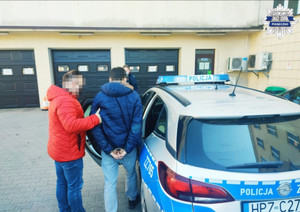 Policjant z zatrzymanym mężczyzną, który wsiada do radiowozu na dziedzińcu komendy