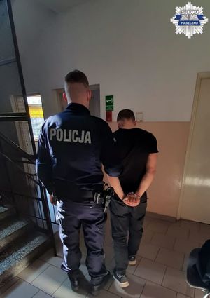 Mężczyzna i policjant stojący tyłem do obiektywu. Zatrzymany ma kajdanki założone na ręce