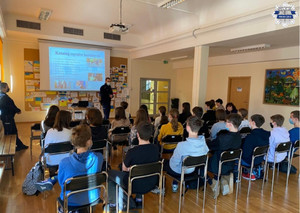 Policjant stoi przy tablicy multimedialnej, wyświetlana jest prezentacja dotyczaca odpowiedzialności karnej, uczniowie siedzą na krzesłach w ławkach