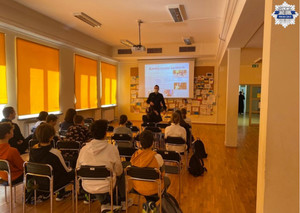 Policjant stoi przy tablicy multimedialnej, wyświetlana jest prezentacja dotyczaca odpowiedzialności karnej, uczniowie siedzą na krzesłach w ławkach