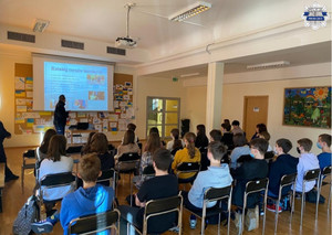 Policjant stoi przy tablicy multimedialnej, wyświetlana jest prezentacja dotyczaca odpowiedzialności karnej, uczniowie siedzą na krzesłach w ławkach