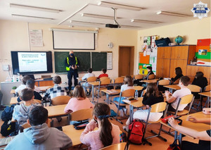 Policjant stoi przy tablicy multimedialnej, wyświetlana jest prezentacja dotyczaca odpowiedzialności karnej, uczniowie siedzą na krzesłach w ławkach