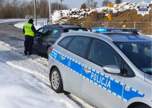 Policjant przy samochodzie, kierujący ma uchyloną szybę w swoim pojeździe, dokonywana jest kontrola stanu trzeźwości za pomocą urządzenia