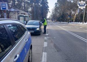 Policjant przy samochodzie, kierujący ma uchyloną szybę w swoim pojeździe, dokonywana jest kontrola stanu trzeźwości za pomocą urządzenia