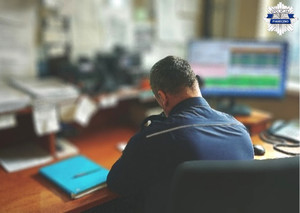 policjant dyżurny siedzący przy swoim biurku ze słuchawką telefonu, rozmawiający