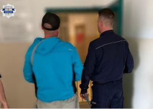 Policjant z zatrzymanym mężczyzną przy wejściu do pomieszczenia dla osób zatrzymanych, stoją tyłem