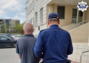 Policjant z zatrzymanym mężczyzną przed siedzibą komendy