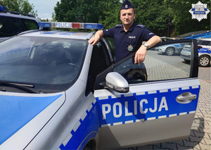 Umundurowany policjant stoi przy radiowozie