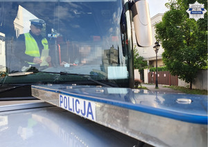 Policjant kontrolujący kierowcę autokaru, w tle napis policja z radiowozu