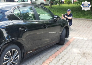 Policjantka wykonująca zdjęcia pojazdu, pojazd jest poddawany oględzinom, zaparkowany na parkingu niestrzeżonym