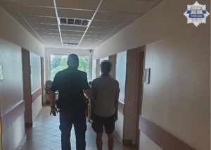 umundurowany policjant z zatrzymanym mężczyznom, stoją tyłem, zdjęcie na korytarzu jednostki policji