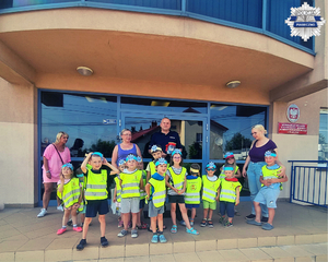 Zdjęcie grupowe policjanta i dzieci na tle budynku komisariatu