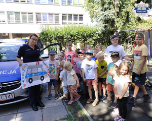 Policjantka wraz z dziećmi na tle radiowozu, zdjęcie grupowe