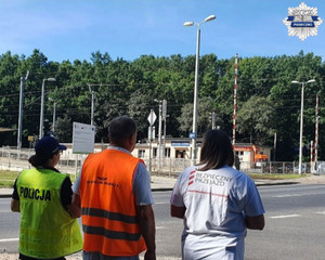 policjantka oraz przedstawiciele PKP PLK na tle przejazdu kolejowego