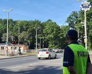 Policjant stojący w okolicy przejazdu kolejowego obserwujący zachowania kierowcow i pieszych