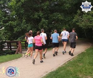 Grupa osób w strojach sportowych biegnąca razem do po ścieżce biegowej.