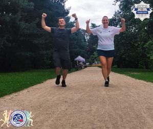 Dwie osoby w strojach sportowych biegną po ścieżce biegowej. Mają uniesione ręce do góry w geście radości.