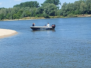 Po wodzie płynie łódź motorowa policyjna, w której jest dwóch umundurowanych policjantów. Jeden funkcjonariusz jest z policji rzecznej a drugi to dzielnicowy.