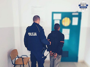 Policjant z zatrzymanym mężczyzną na tle wejścia do pomieszczenia dla osób zatrzymanych