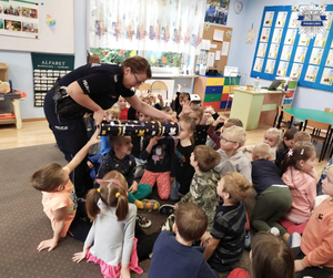 Policjanta pokazuje dzieciom &quot;magiczną tubę&quot;, dzieci siedzą na dywanie