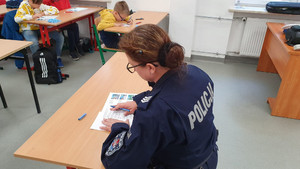 Umundurowana policjantka siedzi w ławce szkolnej i sprawca karty testów.