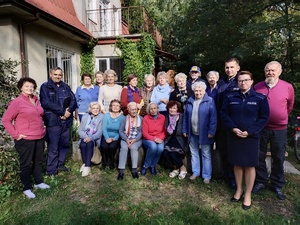 Na zdjęciu jest grupa starszych osób a wśród nich stoją dwaj umundurowani policjanci i jedna policjanta również w mundurze.