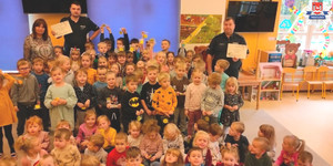 Zdjęcie grupowe policjantów dzielnicowych z przedszkolakami. Dzieci uśmiechają się, trzymają odblaski, policjanci trzymają dyplomy, które otrzymali w podziękowaniu za spotkanie