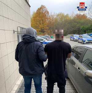 Policjant z zatrzymanym mężczyzną, na placu przed jednostką policji